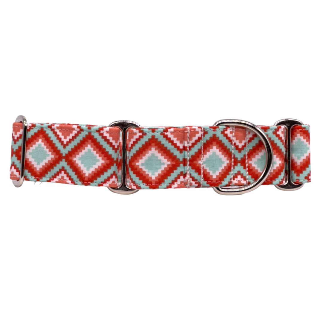 A martingale dog collar with a geometric pattern in shades of turquoise, coral, and white. The design includes diamond and zigzag shapes, and the collar is fitted with two shiny silver metal rings and an adjustable slider.